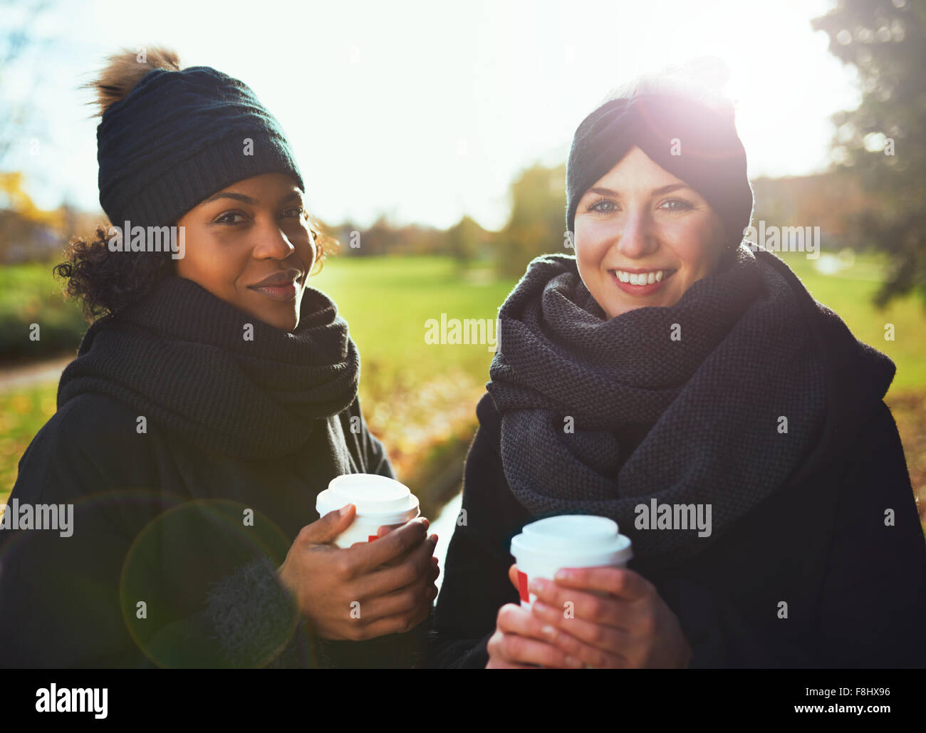 Zwei junge Frauen Blick in die Kamera, lächelnd Kaffee gegen herbstliche Park gehen mit gedrückter Stockfoto