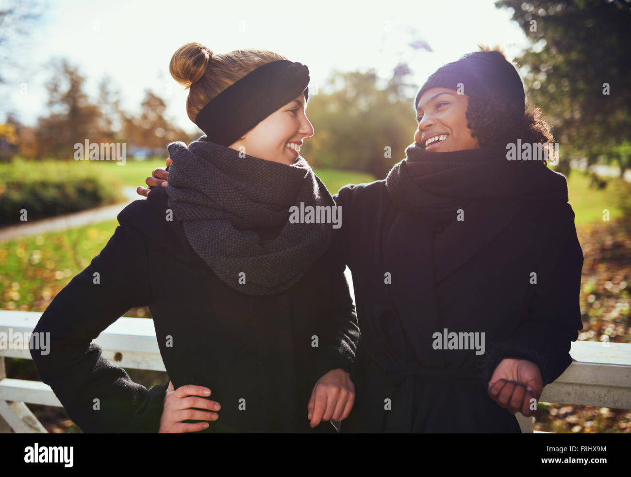 Zwei Freundinnen sahen einander und lächelt, steht auf der Brücke im park Stockfoto