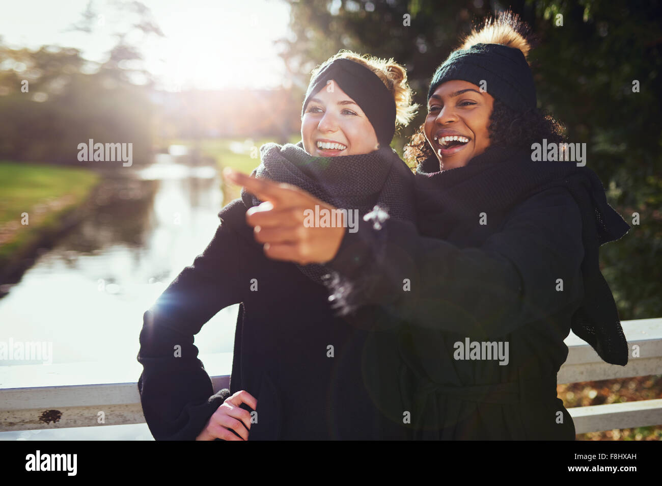 Zwei Freundinnen lachend an etwas beim Stehen in der Park gegen des Flusses. Stockfoto