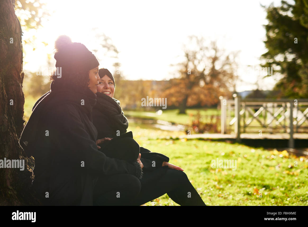 Zwei junge Frauen sitzen im herbstlichen Park, stützte sich auf Baumstamm. Sonnigen Stockfoto