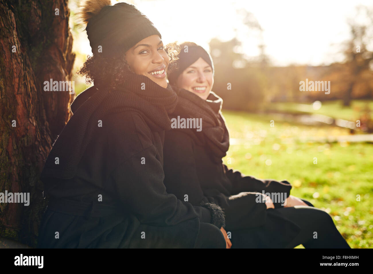 Zwei junge Frauen sitzen im herbstlichen Park und lächelt in die Kamera. Sonnig Stockfoto