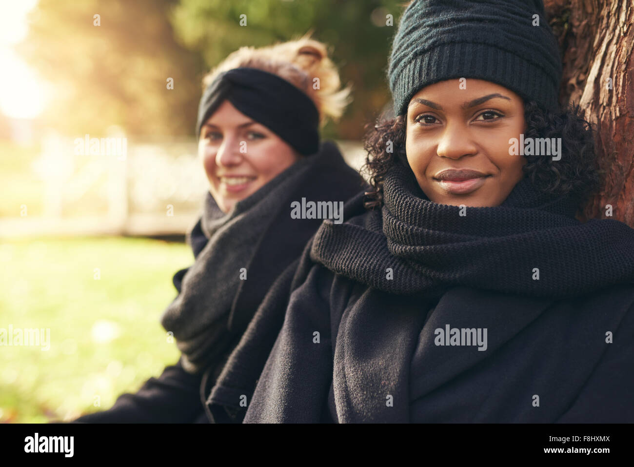 Nahaufnahme von zwei lächelnde junge Frauen stützte sich auf Baumstamm im herbstlichen park Stockfoto