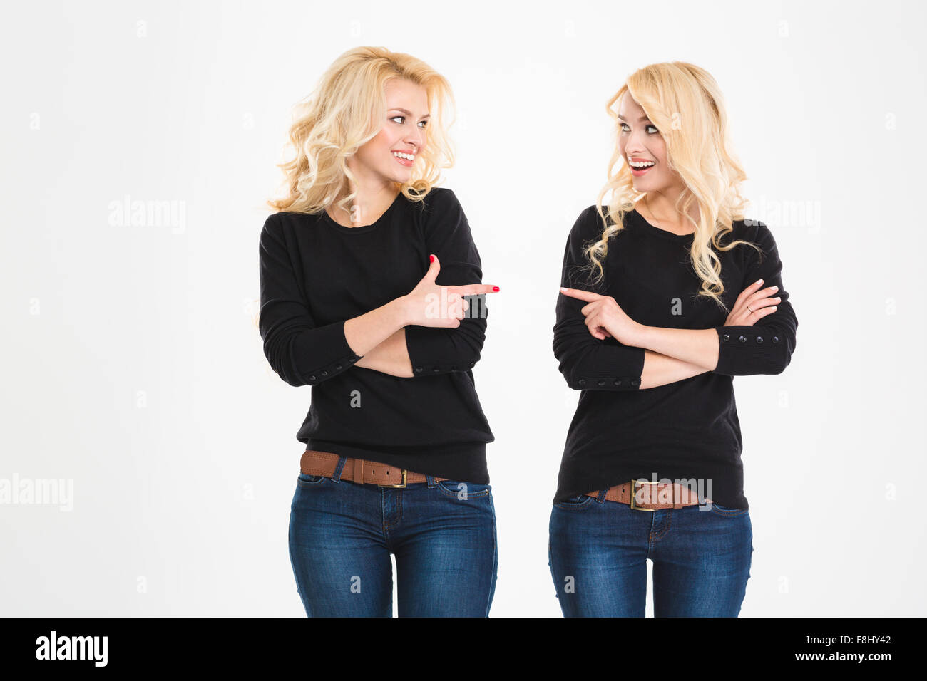 Zwei Schwestern fröhlich Attrative Zwillinge zeigen und sahen einander auf weißem Hintergrund Stockfoto
