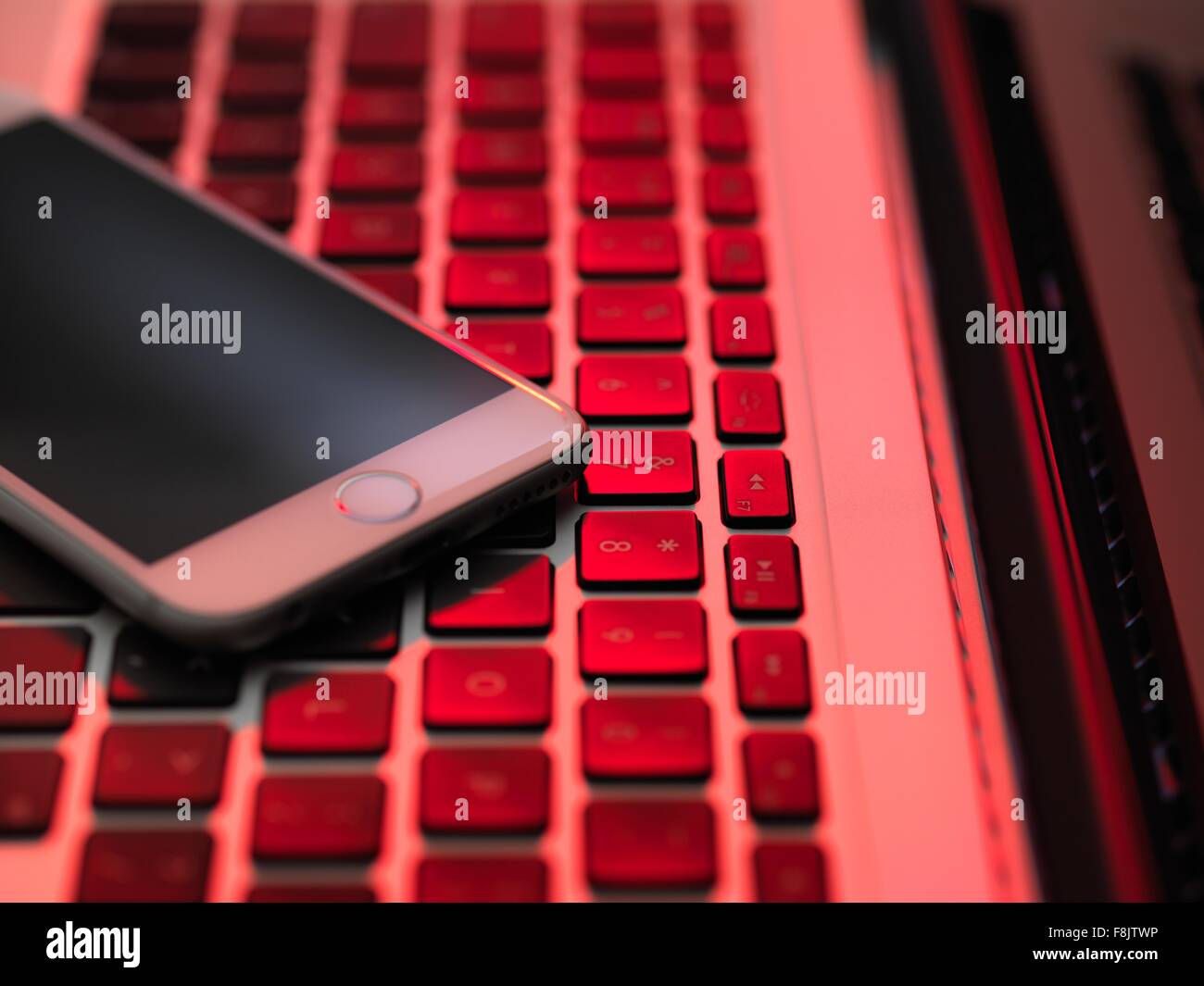 Erhöhte Ansicht von Handy auf Computer-Tastatur in rotes Licht Stockfoto