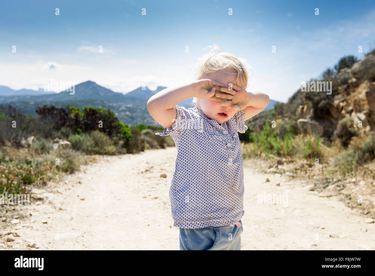 Weiblichen Kleinkind auf Feldweg mit Händen über Augen, Calvi, Korsika, Frankreich Stockfoto
