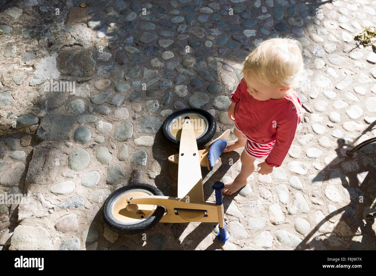 Draufsicht der weiblichen Kleinkind und hölzernen Fahrrad auf Kopfsteinpflaster Stockfoto