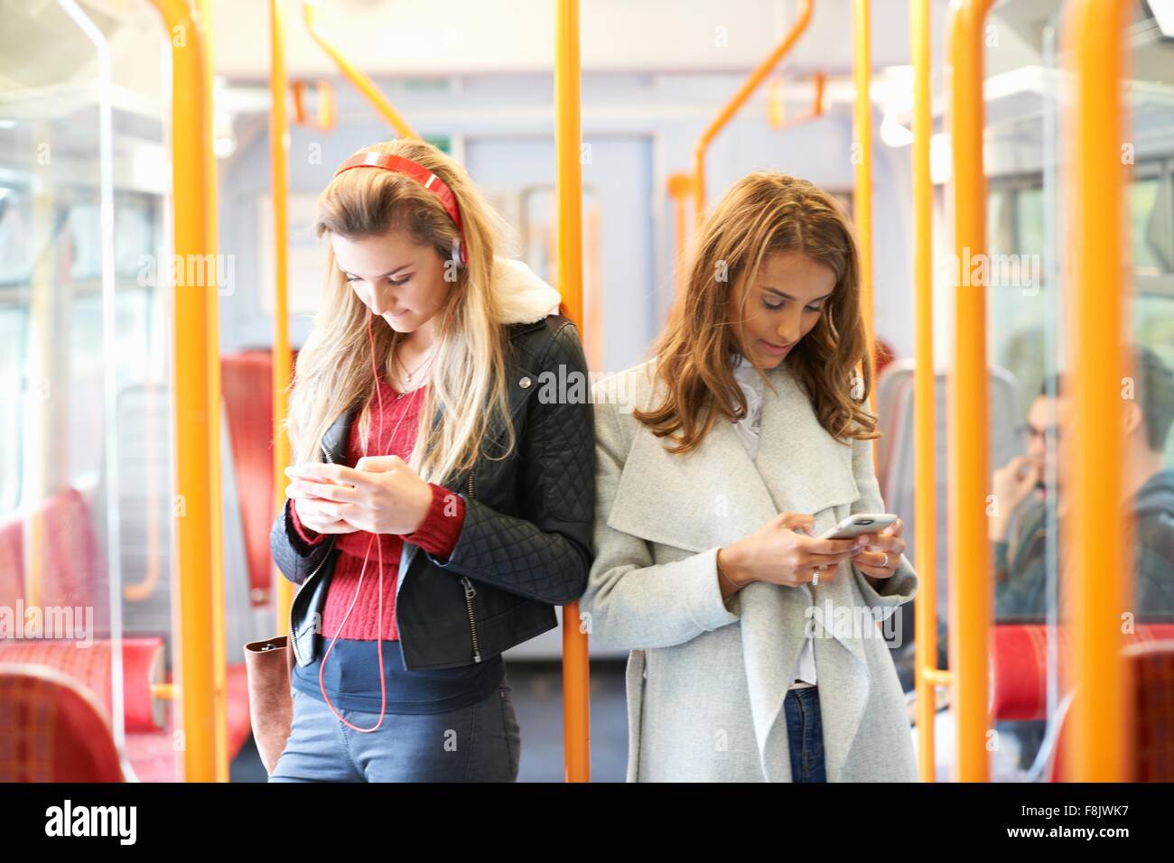 Zwei junge Frauen auf Zug, Rücken an Rücken mit smartphones Stockfoto