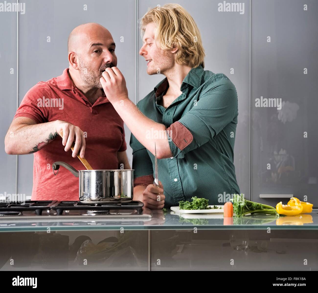 Romantisches männliche paar schmeckendes Essen, während in Küche kochen Stockfoto