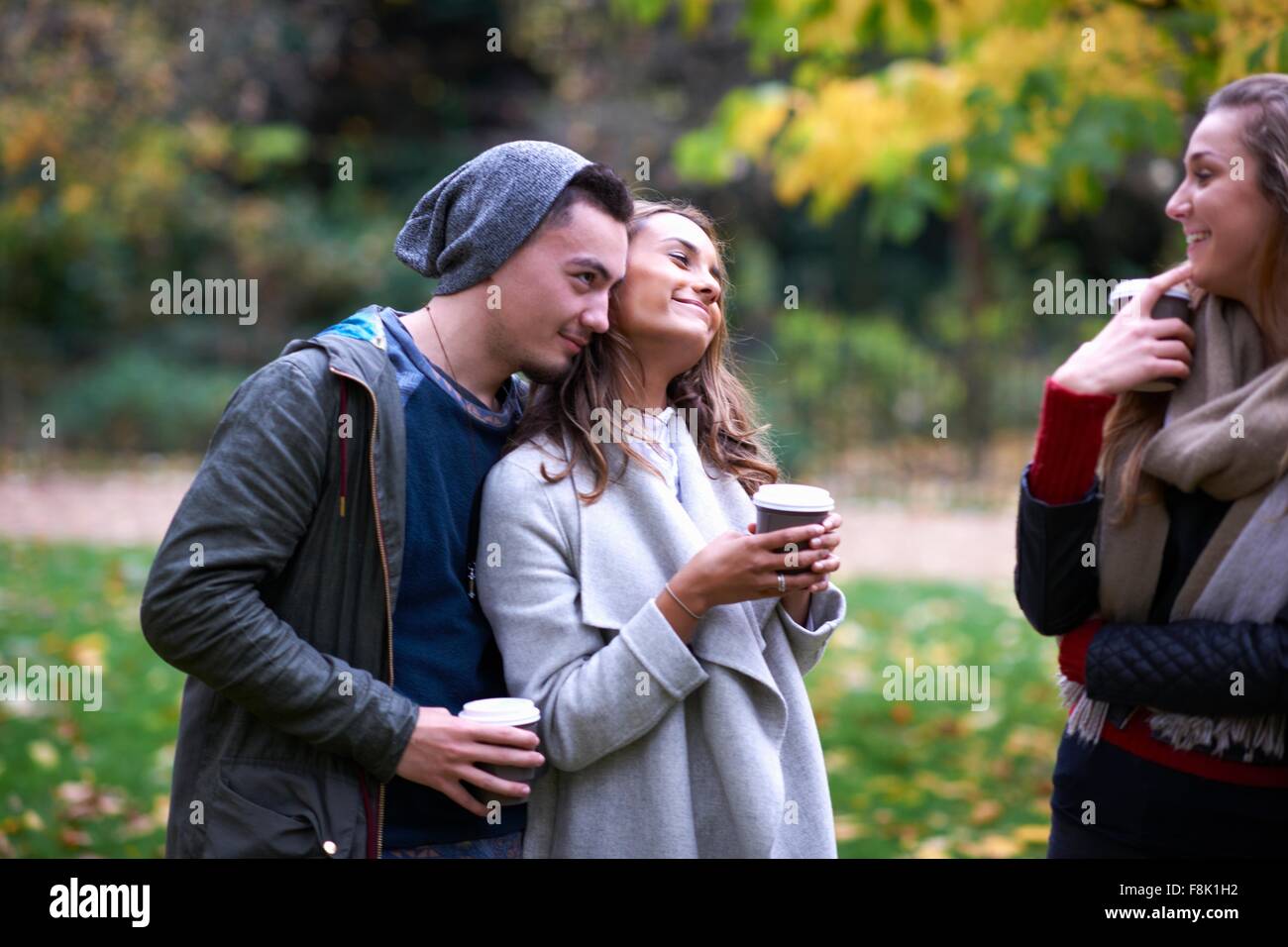 Jungen Erwachsenen Freunden plaudern und trinken Kaffee zum mitnehmen im Herbst park Stockfoto
