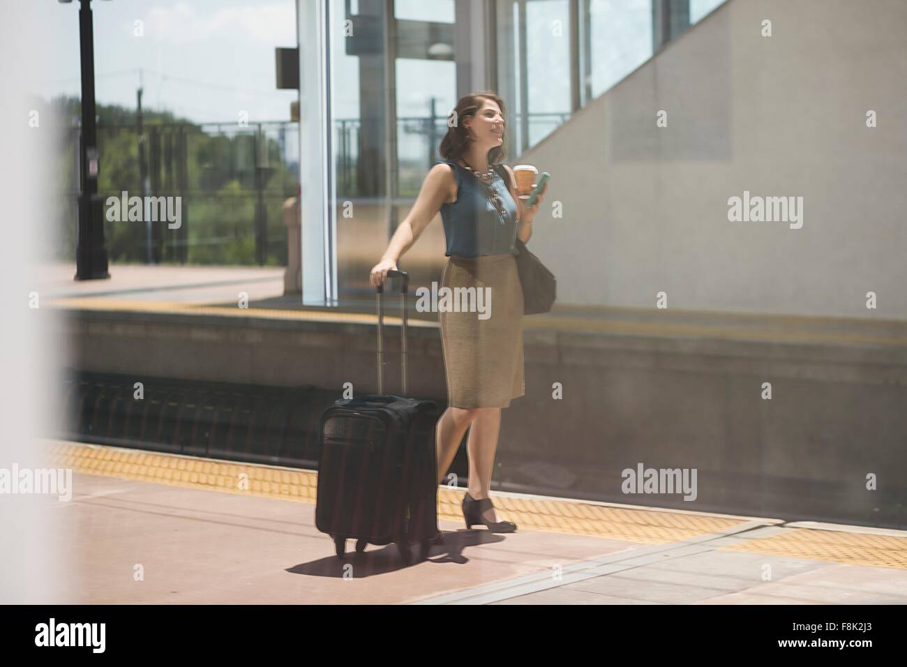 Mitte erwachsenen Frau wartet am Bahnhof, mit fahrbaren Koffer und Kaffeetasse Stockfoto