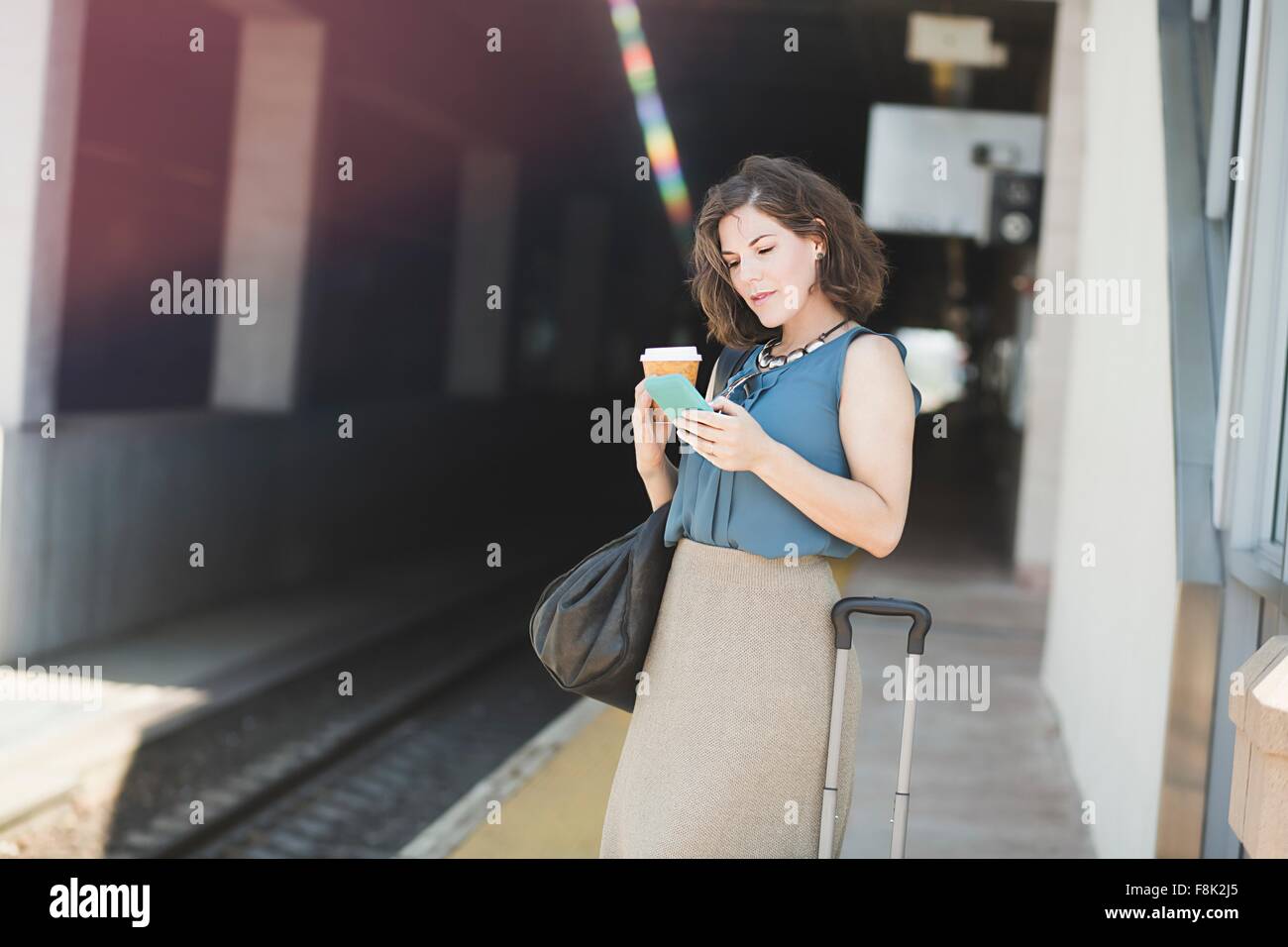 Mitte erwachsenen Frau wartet am Bahnhof, mit Smartphone, halten Kaffeetasse Stockfoto
