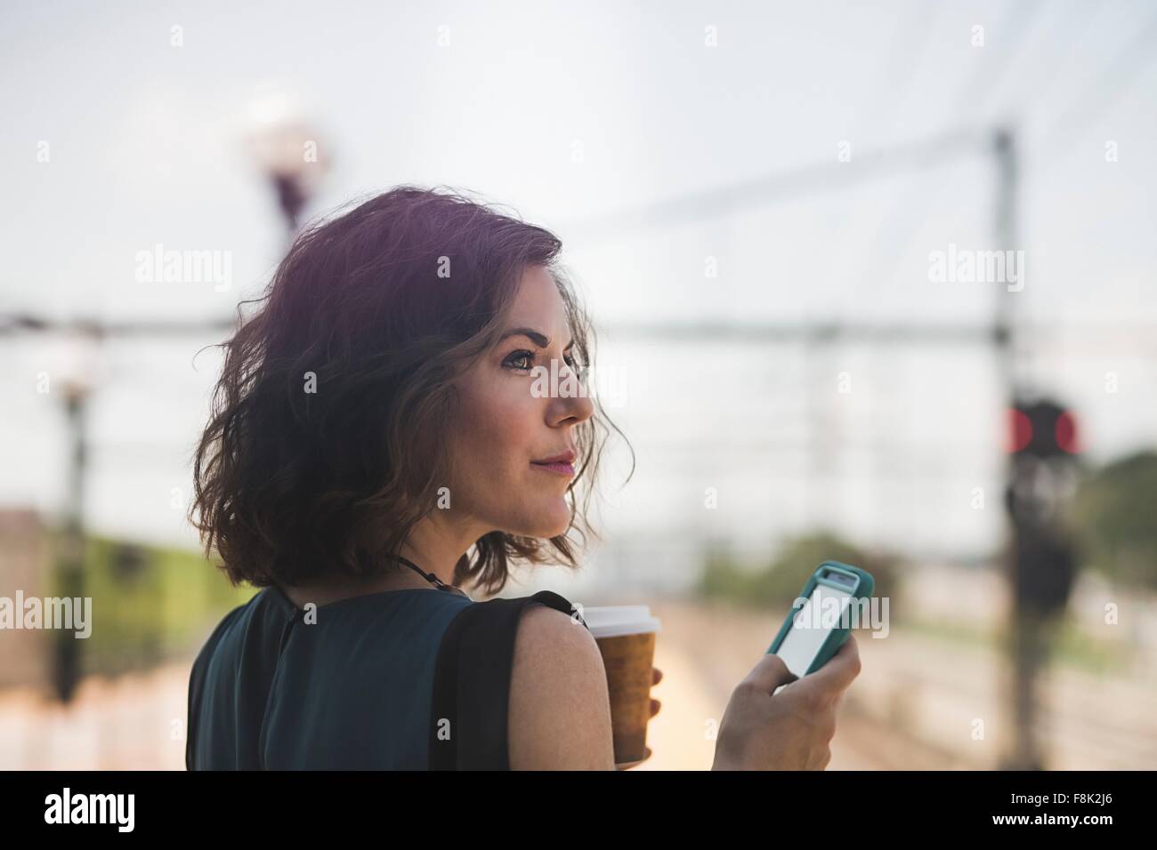 Mitte erwachsenen Frau wartet am Bahnhof, mit Smartphone, halten Kaffeetasse Stockfoto