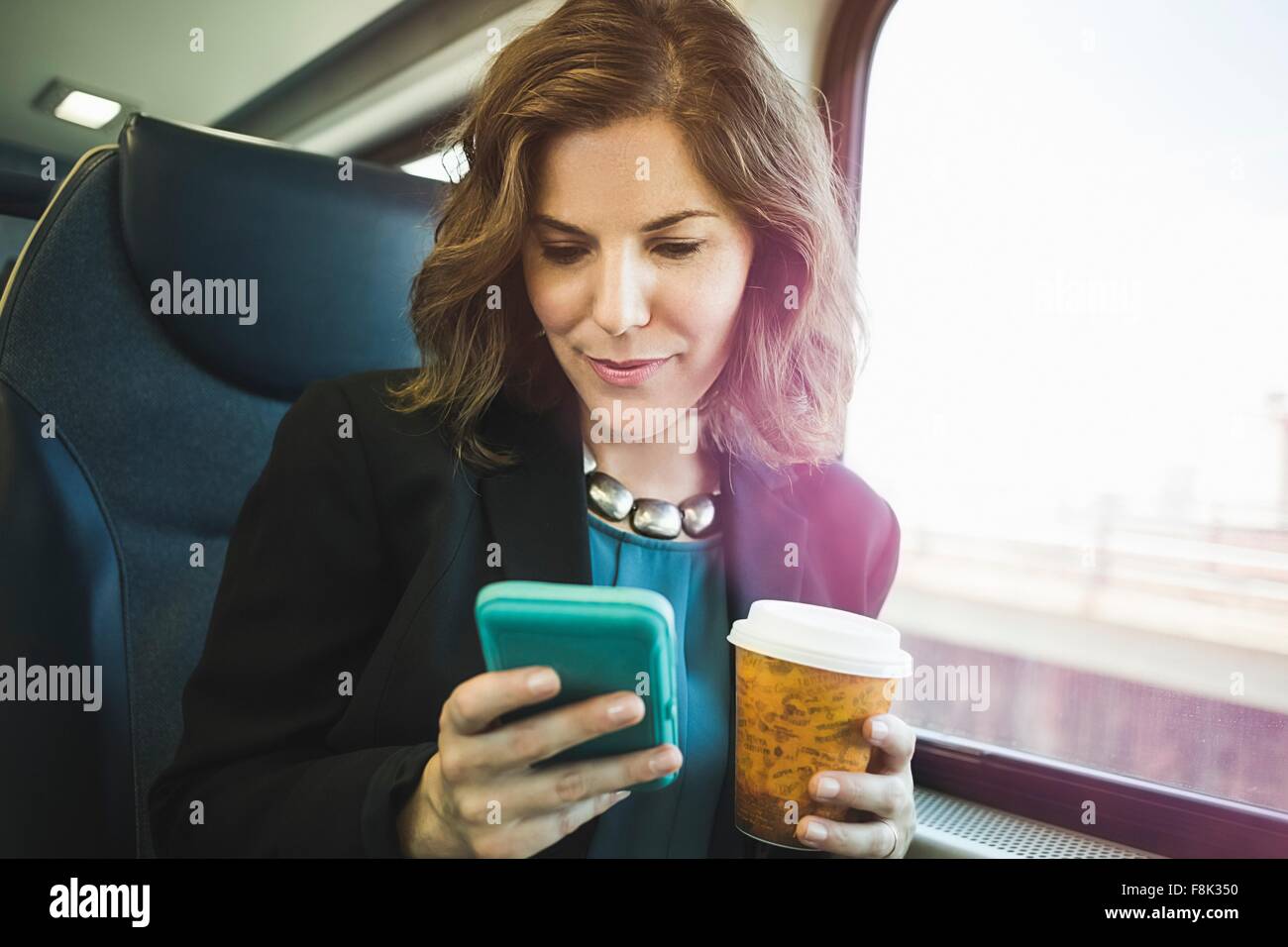 Mitte Erwachsene Frau in Zug, mit Smartphone, halten Kaffeetasse Stockfoto