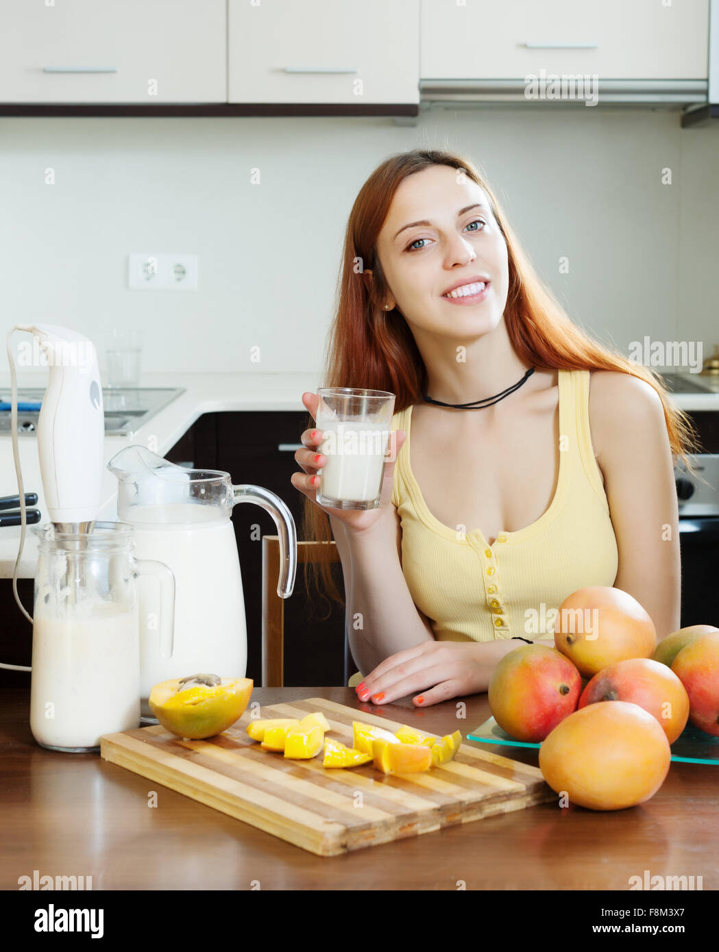 gewöhnliche Frau trinkt Milchshake mit Mango und Milch am heimischen Küche Stockfoto