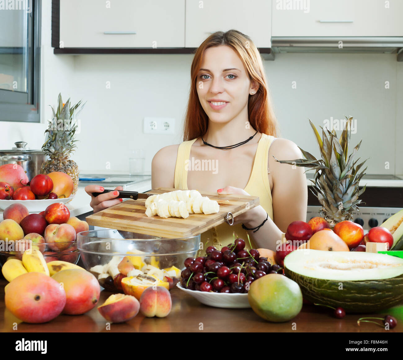 Positiven langhaarige Frau macht Obstsalat mit Banane in der Küche zu Hause Stockfoto