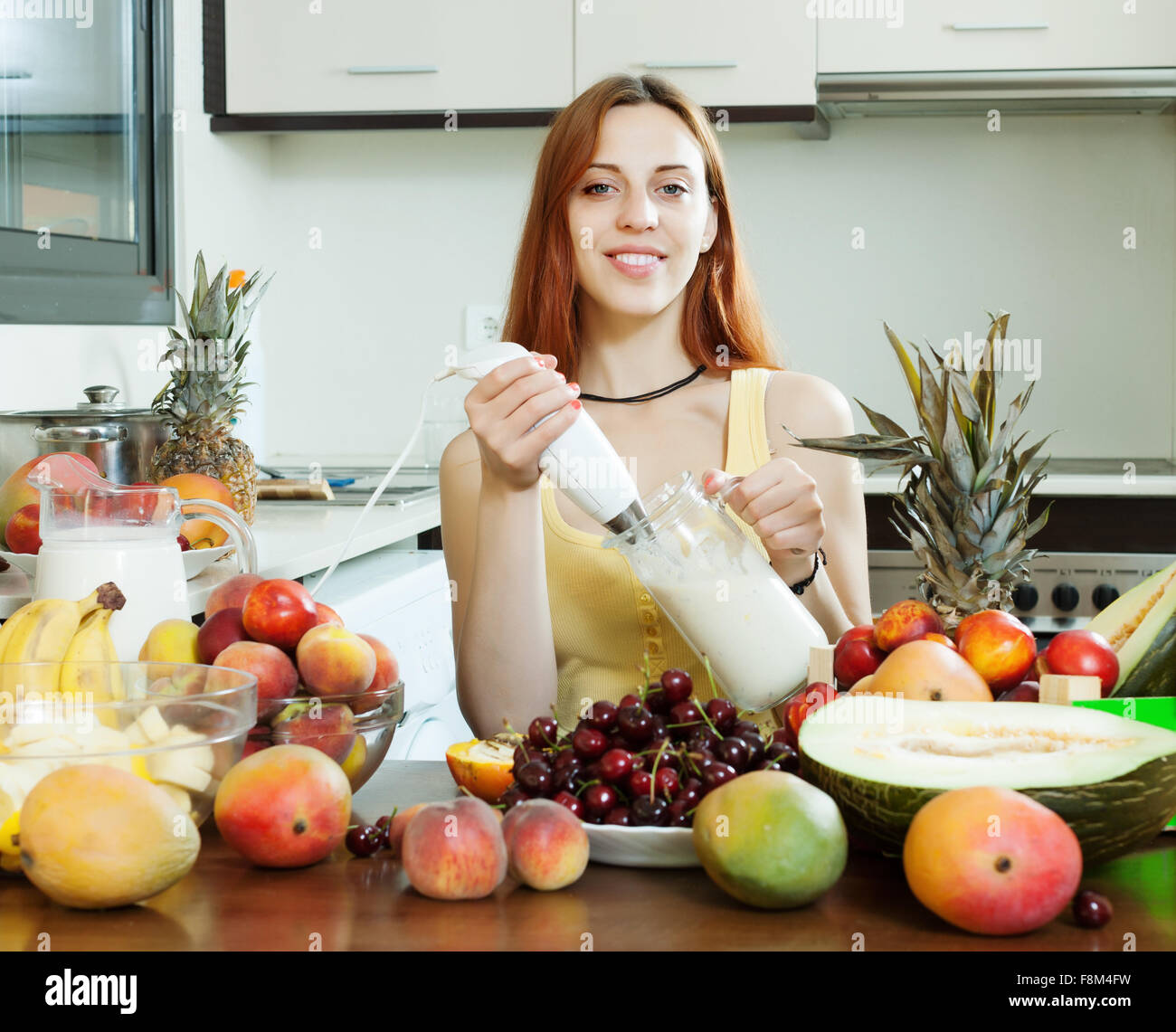 gewöhnliche Frau Milchshake mit Früchten und Milch in der heimischen Küche kochen Stockfoto