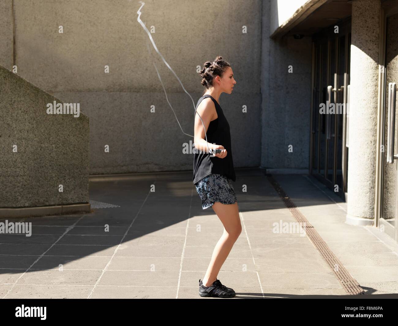 Junge Frau, die neben Gebäude überspringen Stockfoto