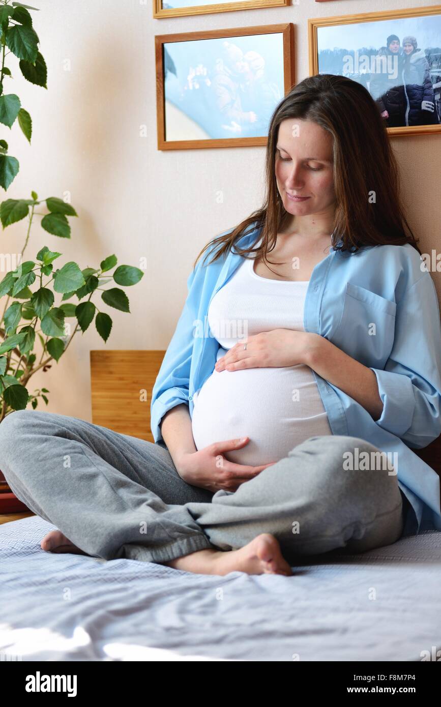 Schwangere Frau sitzt auf dem Bett, hält Magen Stockfoto