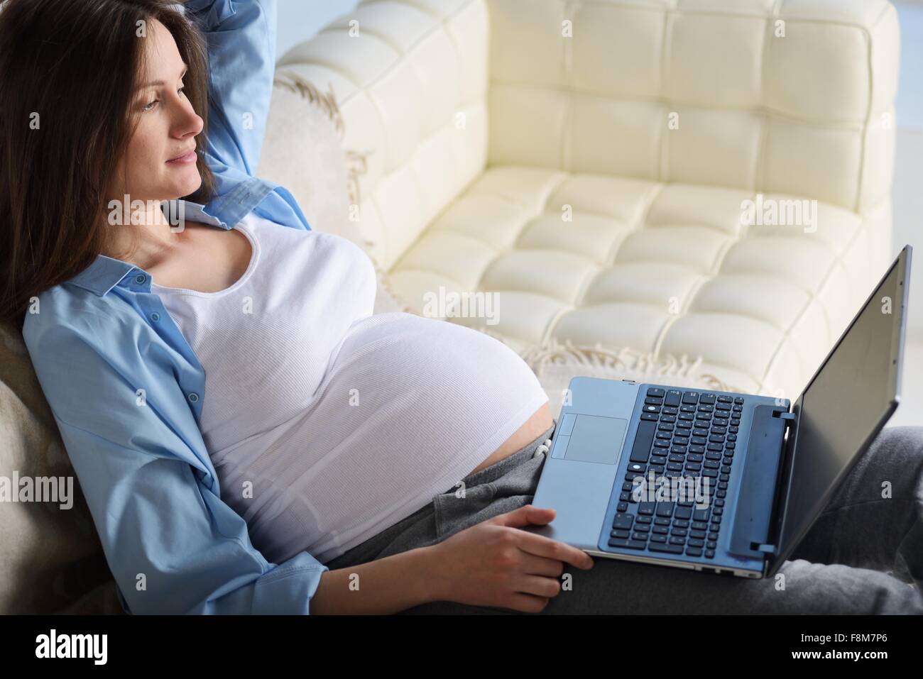 Schwangere Frau sitzt auf dem Sofa, mit laptop Stockfoto