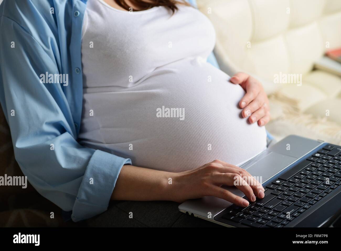 Schwangere Frau sitzt auf dem Sofa, mit Laptop, Mittelteil Stockfoto