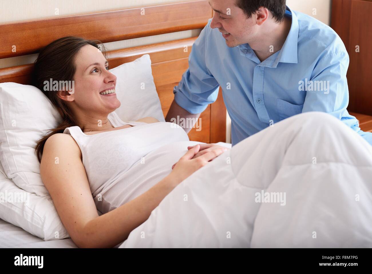 Schwangere Frau im Bett liegend, Mann neben ihr sitzen Stockfoto