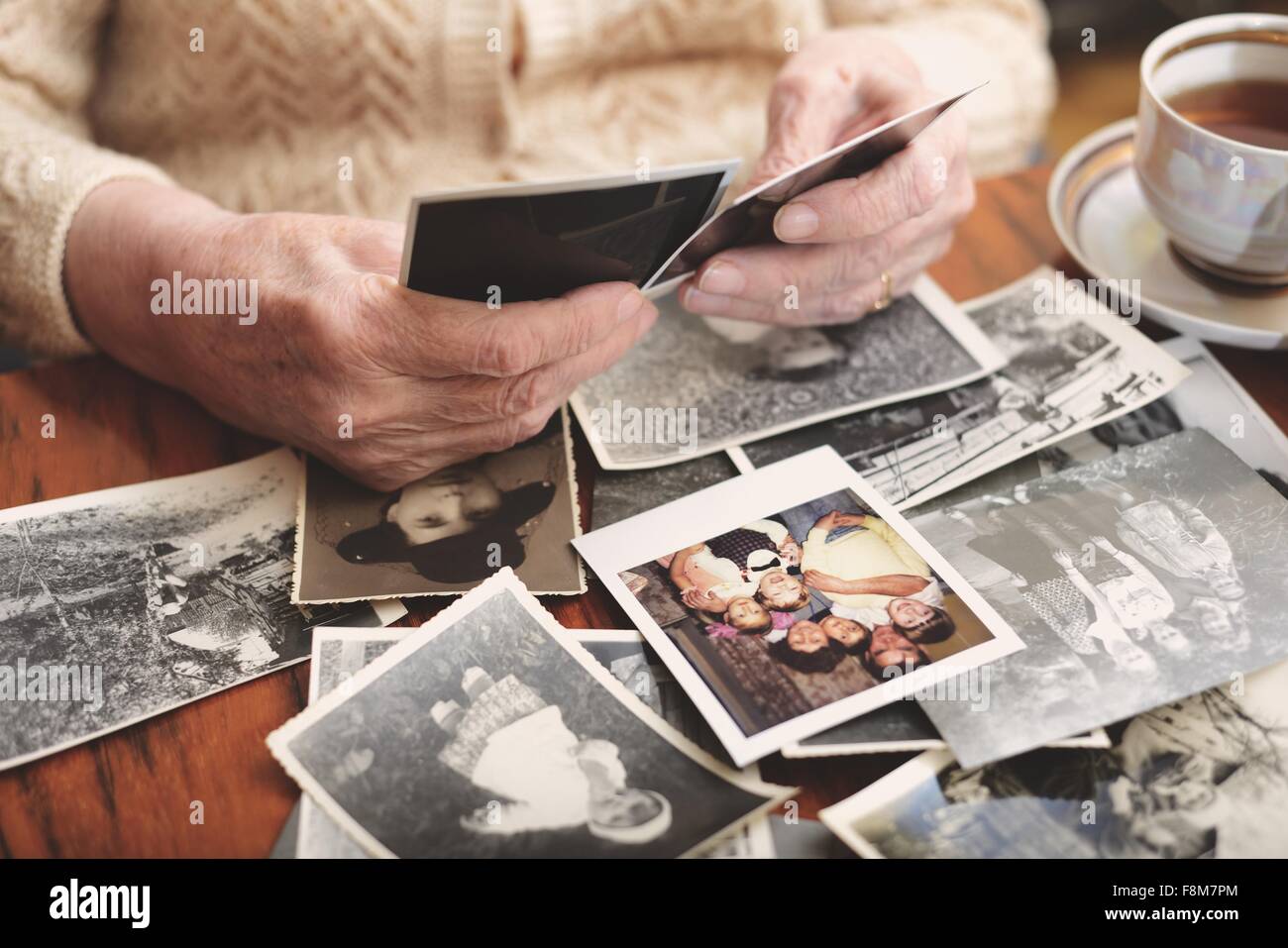 Ältere Frau sitzt am Tisch, Blick durch alte Fotografien, Mittelteil Stockfoto