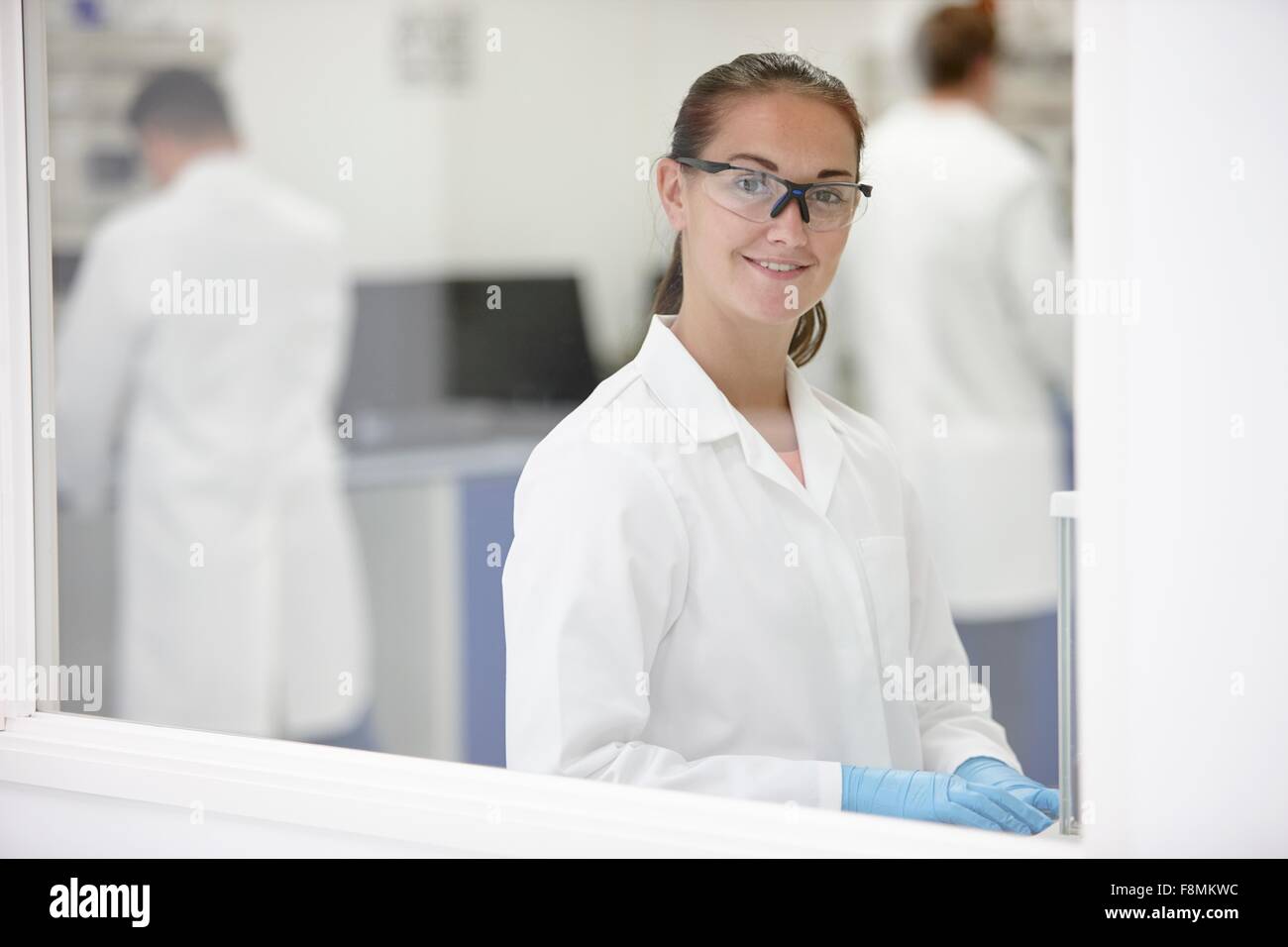 Wissenschaftler, die lächelnd im Labor, im Hintergrund arbeitenden Kolleginnen und Kollegen Stockfoto
