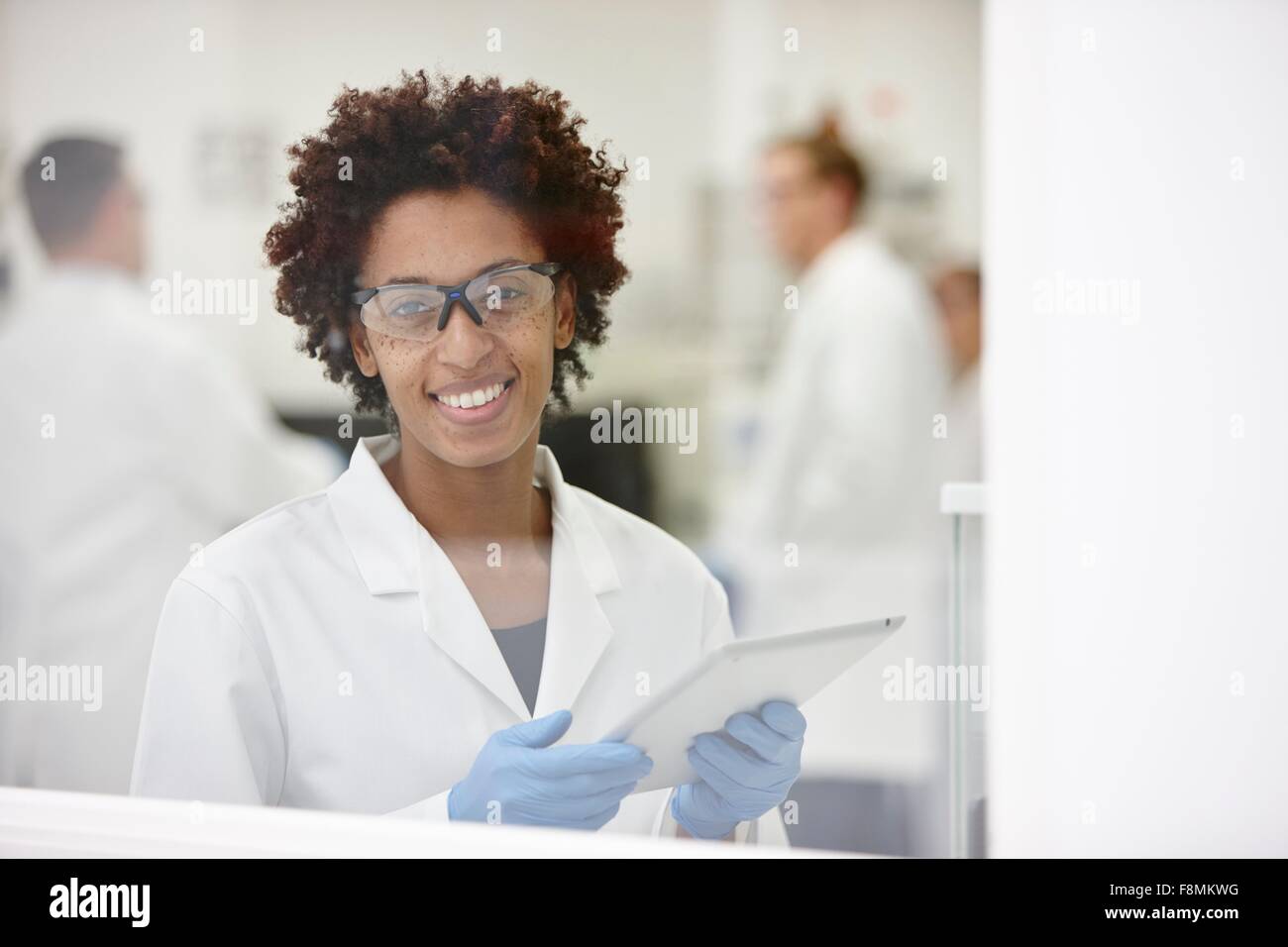 Wissenschaftler, die lächelnd im Labor, im Hintergrund arbeitenden Kolleginnen und Kollegen Stockfoto