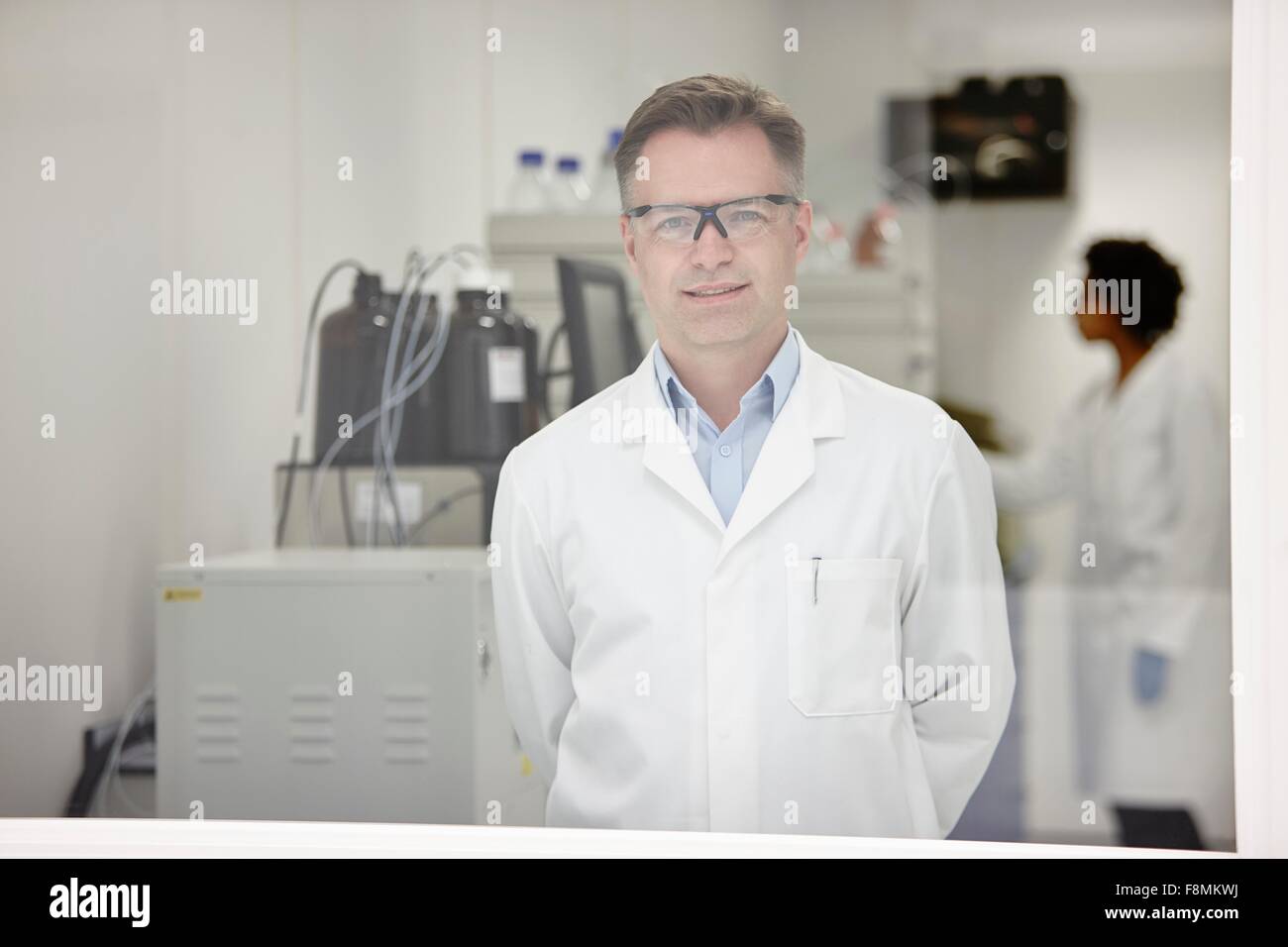 Wissenschaftler im Labor, Kollege im Hintergrund arbeitet, lächelnd Stockfoto