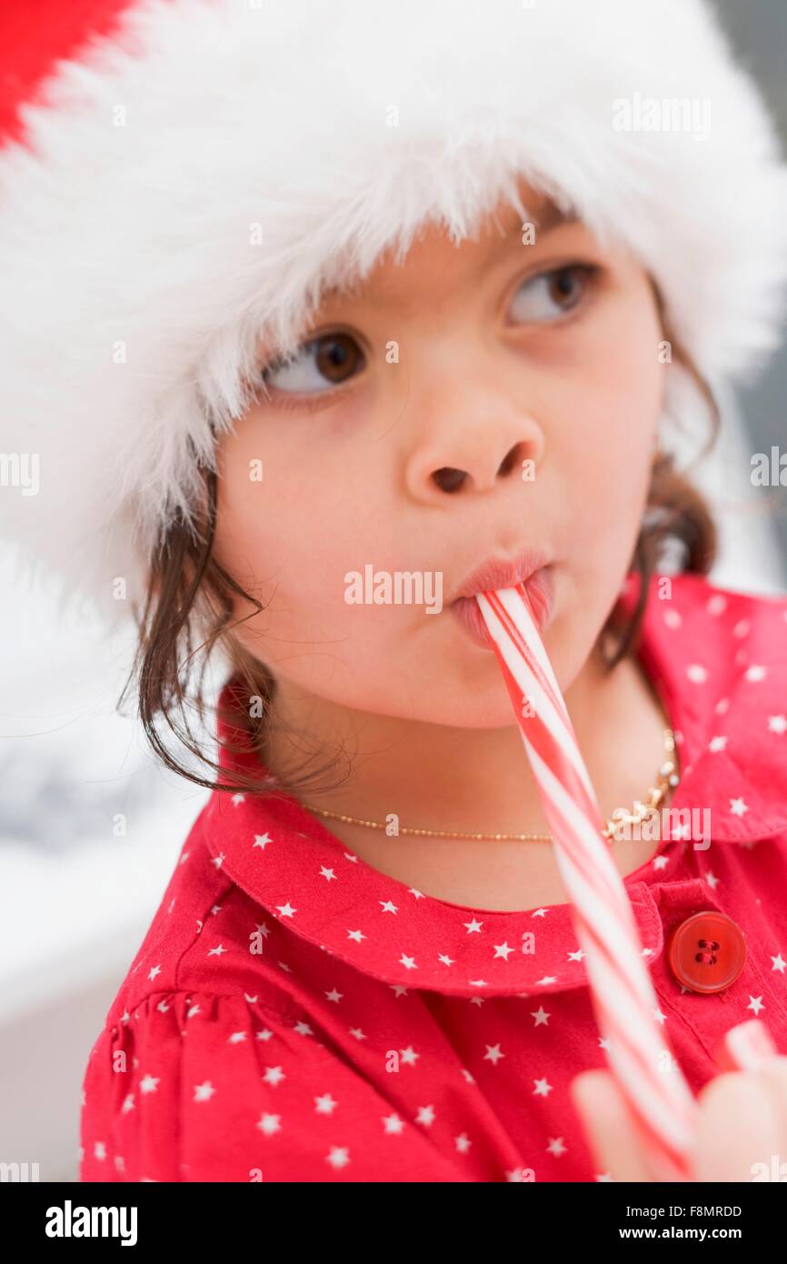 Kleines Mädchen in Weihnachtsmann Hut Essen Zuckerstange Stockfoto