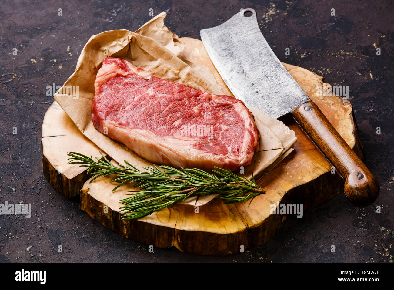 Rohes Frischfleisch Striploin Steak und Fleischerbeil auf Butcher-Block auf dunklem Hintergrund Stockfoto