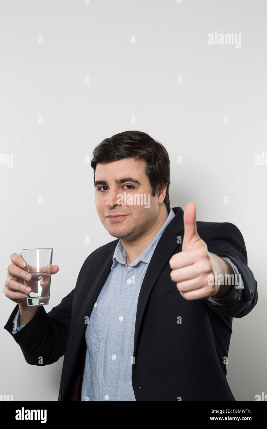 Dunkelhaarige Europäische Geschäftsmann mit einem frechen Look gibt einen klopft-Up mit einem Glas Wasser in der anderen Hand gleichzeitig an einem Stockfoto