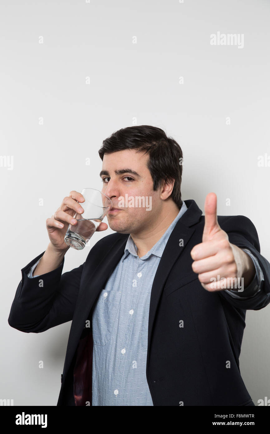 Dunkelhaarige Europäische Geschäftsmann mit einem frechen Look gibt einen klopft-Up beim Trinken aus einem Glas Wasser in der anderen Hand während Stockfoto