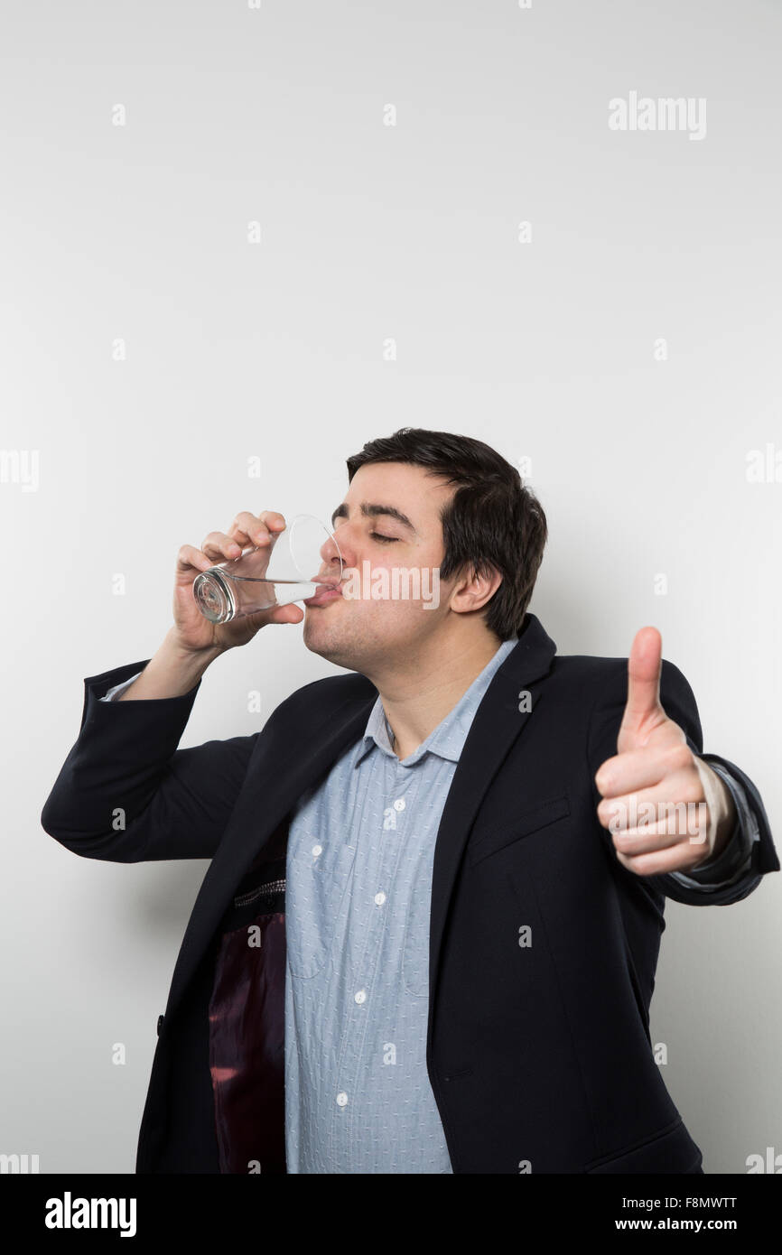 Dunkelhaarige Europäische Geschäftsmann mit einem frechen Look gibt einen klopft-Up beim Trinken aus einem Glas Wasser in der anderen Hand während Stockfoto