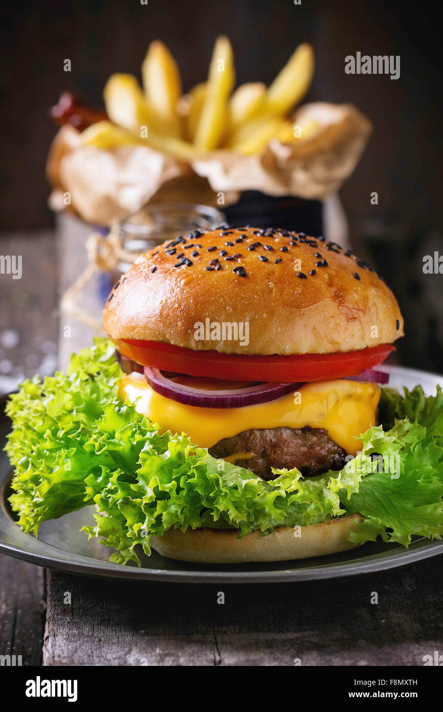 Frische hausgemachte Burger mit schwarzem Sesam auf Holzbrett mit Pommes Frites mit Ketchup-Sauce im Glas serviert Stockfoto
