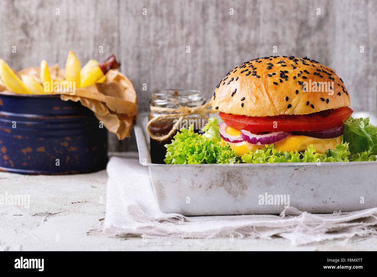 Frische hausgemachte Burger mit schwarzem Sesam in alten Aluminium-Schale mit gegrillten Kartoffeln, mit Ketchup-Sauce im Glas serviert Stockfoto