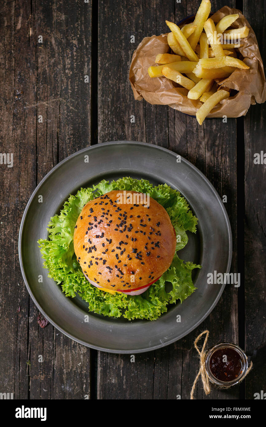 Frische hausgemachte Burger mit schwarzem Sesam auf Metallplatte und Bratkartoffeln in Trägerpapier, serviert mit Ketchup-Sauce in g Stockfoto