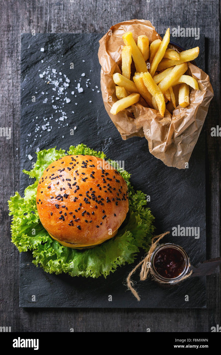 Frische hausgemachte Hamburger mit schwarzem Sesam und Pommes frites Kartoffeln in Schutzpapier, mit Ketchup-Sauce im Glas serviert Stockfoto