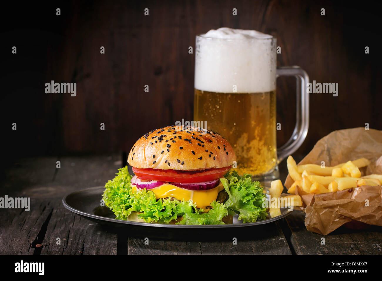 Frische hausgemachte Burger mit in alten Metall-Teller mit Pommes frites in Backpapier, serviert mit Glas kaltes Lager Bier über alte Stockfoto