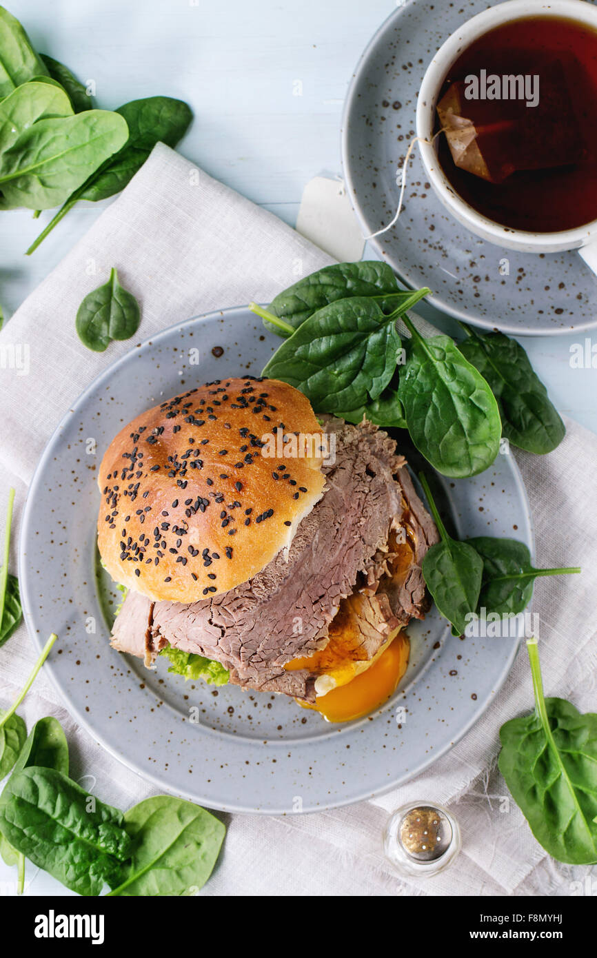 Hausgemachte Sandwich mit gebackenem Fleisch und weich gekochtes Ei, Spinatsalat, Salz und heiße Tasche Tee über blaue Holztisch mit Stockfoto