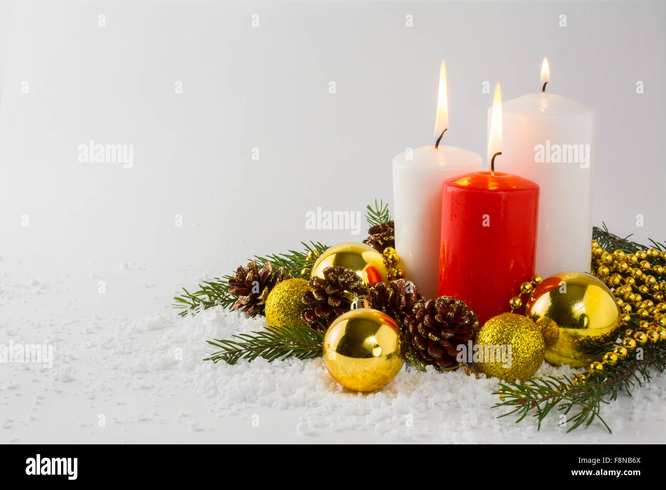 Verbrennung von weißen und roten Weihnachtskerzen, Goldene Kugeln, Tannenzweigen und Zapfen im Schnee auf einem weißen Hintergrund Stockfoto
