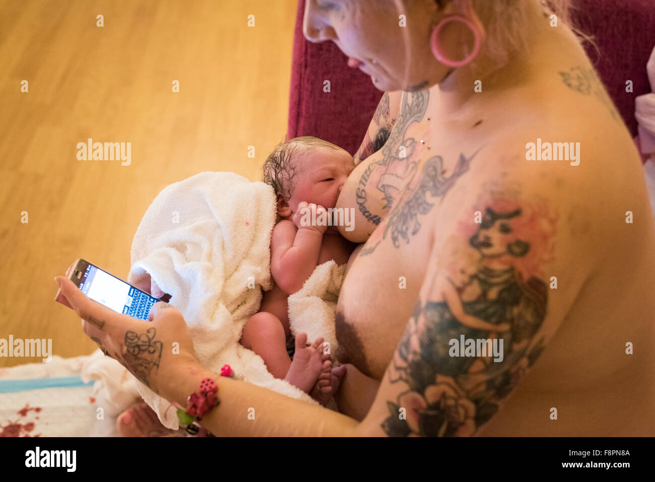 Mutter mit ihr Handy, um Nachricht Freunde während der Stillzeit ihr neugeborenes Kind nach einer ohne fremde Hilfe Hausgeburt (Freebirth). Stockfoto