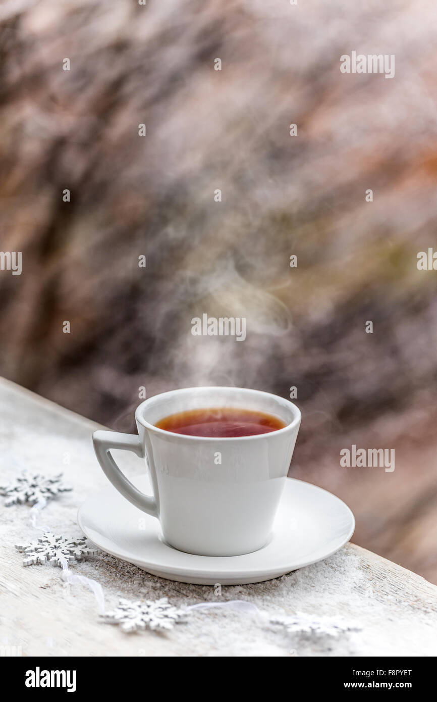 Dampfend heißes Getränk in weiße Tasse auf schneebedeckten Tisch Stockfoto