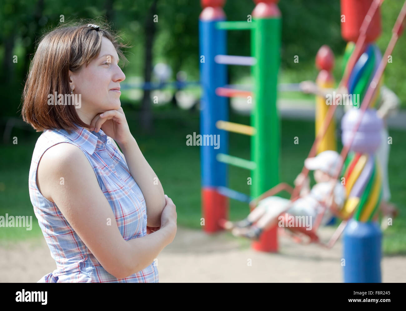 Porträt von Träumerei Frau gegen Kind auf Schaukel auf dem Spielplatz Stockfoto