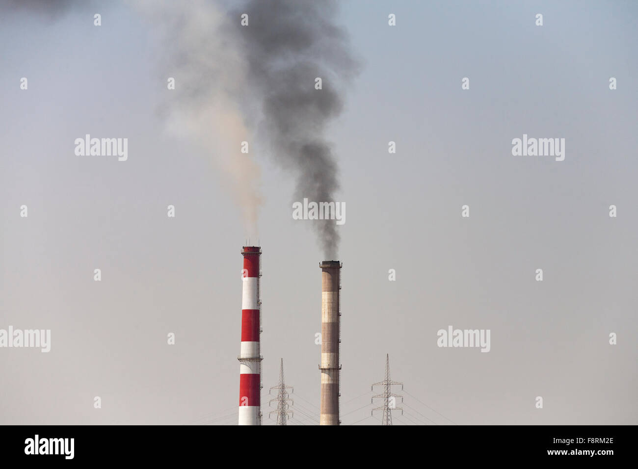 Zwei umweltschädliche Industrieschornsteine und zwei elektrische Masten gegen einen klaren Himmel Stockfoto