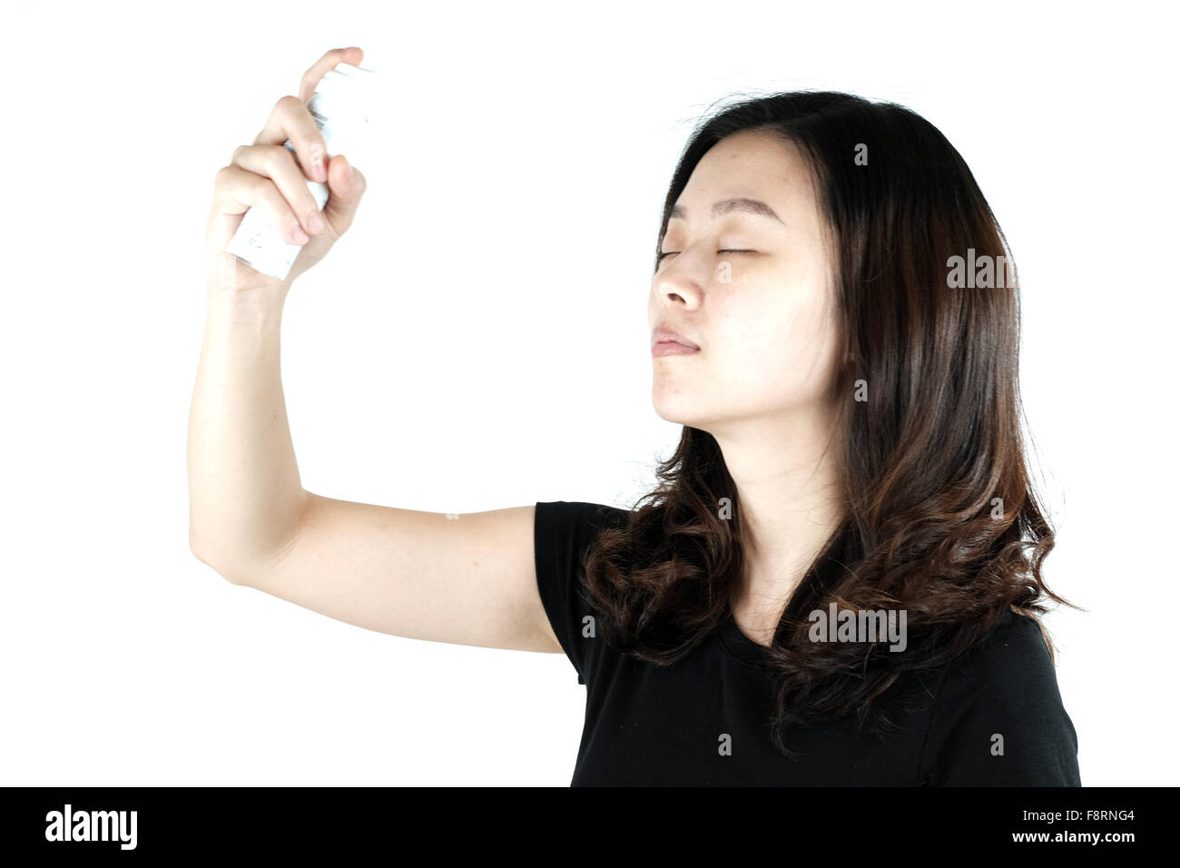 Süße Asiatin mit Gesicht-Spray, isoliert auf weißem Hintergrund Stockfoto