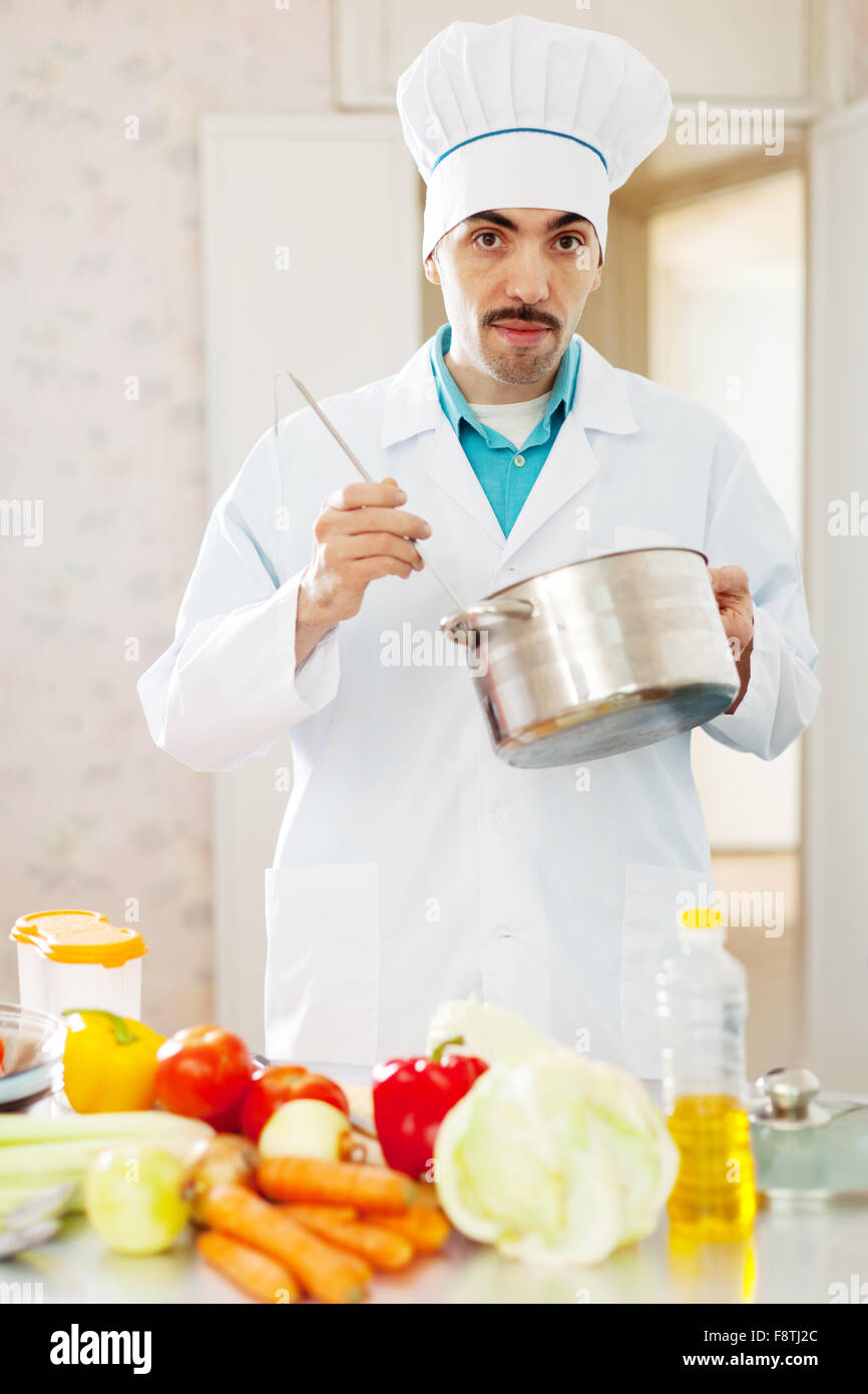 Aucasian Koch Mann Verkostung Suppe mit Schöpfkelle aus der Pfanne in Küche Stockfoto