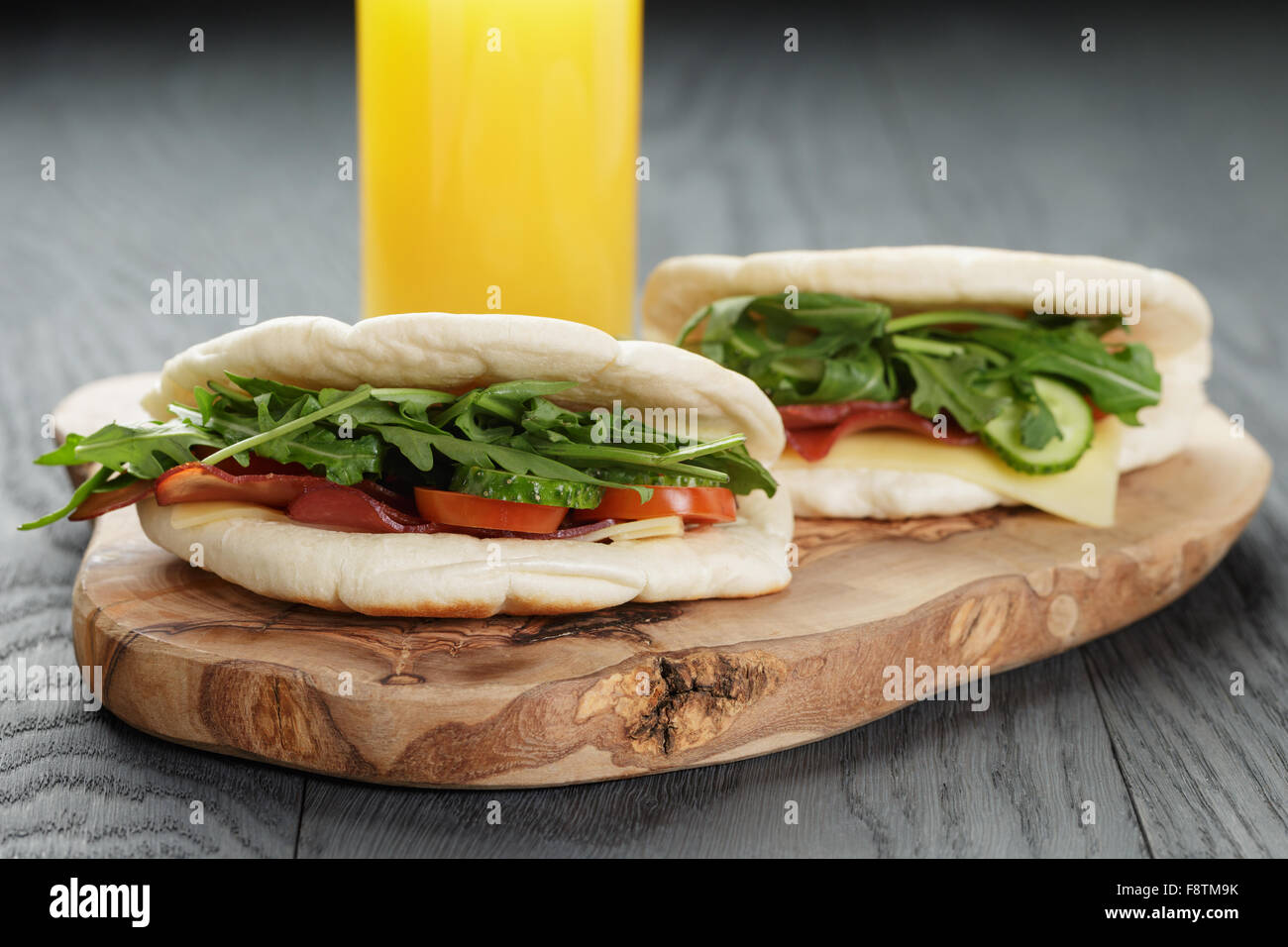 rustikale Sandwiches mit Schinken, Rucola und Tomaten im Fladenbrot auf Holztisch Stockfoto