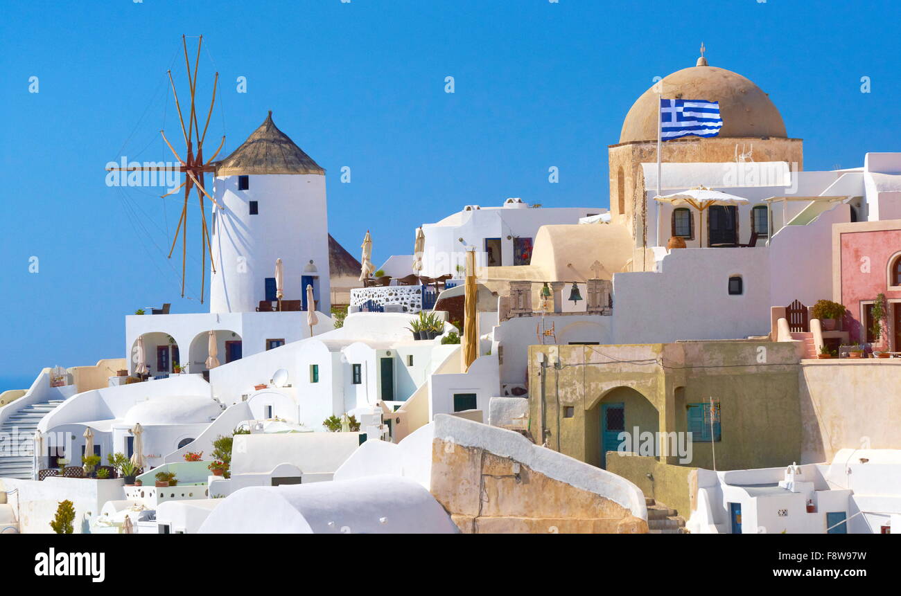 Santorini-Landschaft mit weißen Häusern, Windmühle und griechische Flagge - Stadt Oia, Santorin, Kykladen, Griechenland Stockfoto