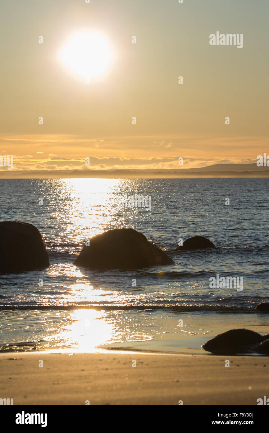 Sonnenuntergang am Strand mit blauem Wasser Felsen und die Reflexion der Sonneneinstrahlung. Stockfoto